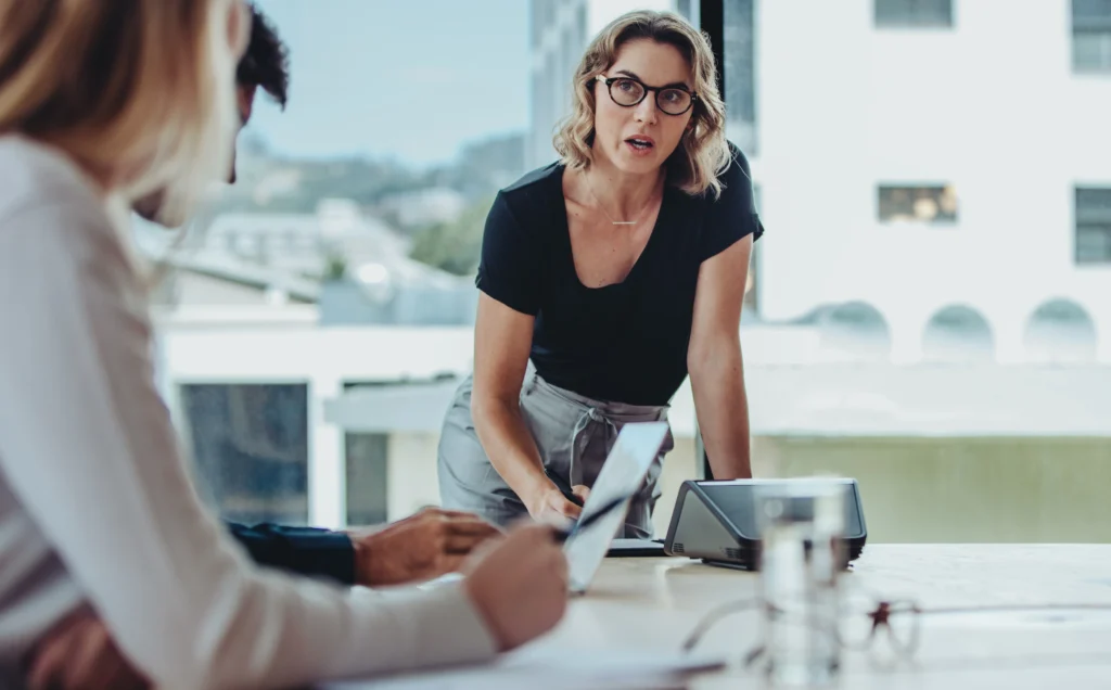 Frau erklärt zwei Kollegen im Meeting einen Sachverhalt auf einem Tablet